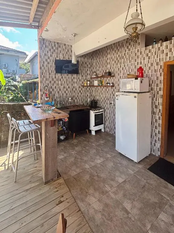 Bar e cozinha com bancada, banquetas e TV